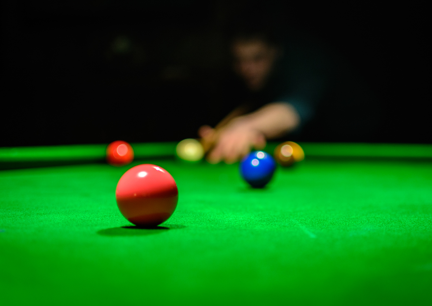 A commercial-style close-up image of a snooker table with a person taking a shot.