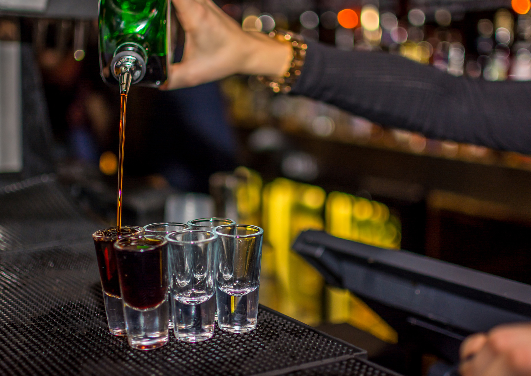 A close-up image of a person pouring alcohol shots at a bar.